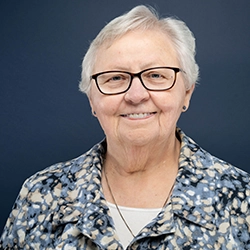 Sister Susan O'Connor smiles into the camera against a dark blue background.